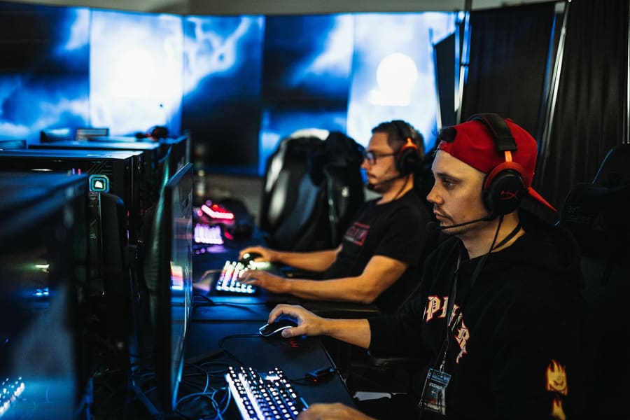 Two players at their PCs, one in a red headset, RGB keyboards glowing
